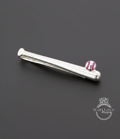 A silver tie clip with a baseball design on it, placed on a dark background.