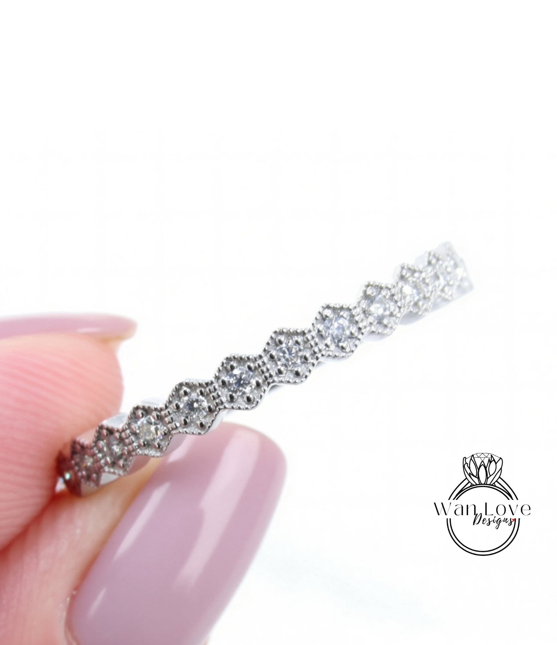 A close-up image of a person's hand holding a silver ring with a row of small diamonds on it.