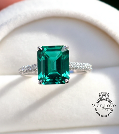 A close-up image of a diamond engagement ring with a large, vibrant green gemstone set in a silver band.