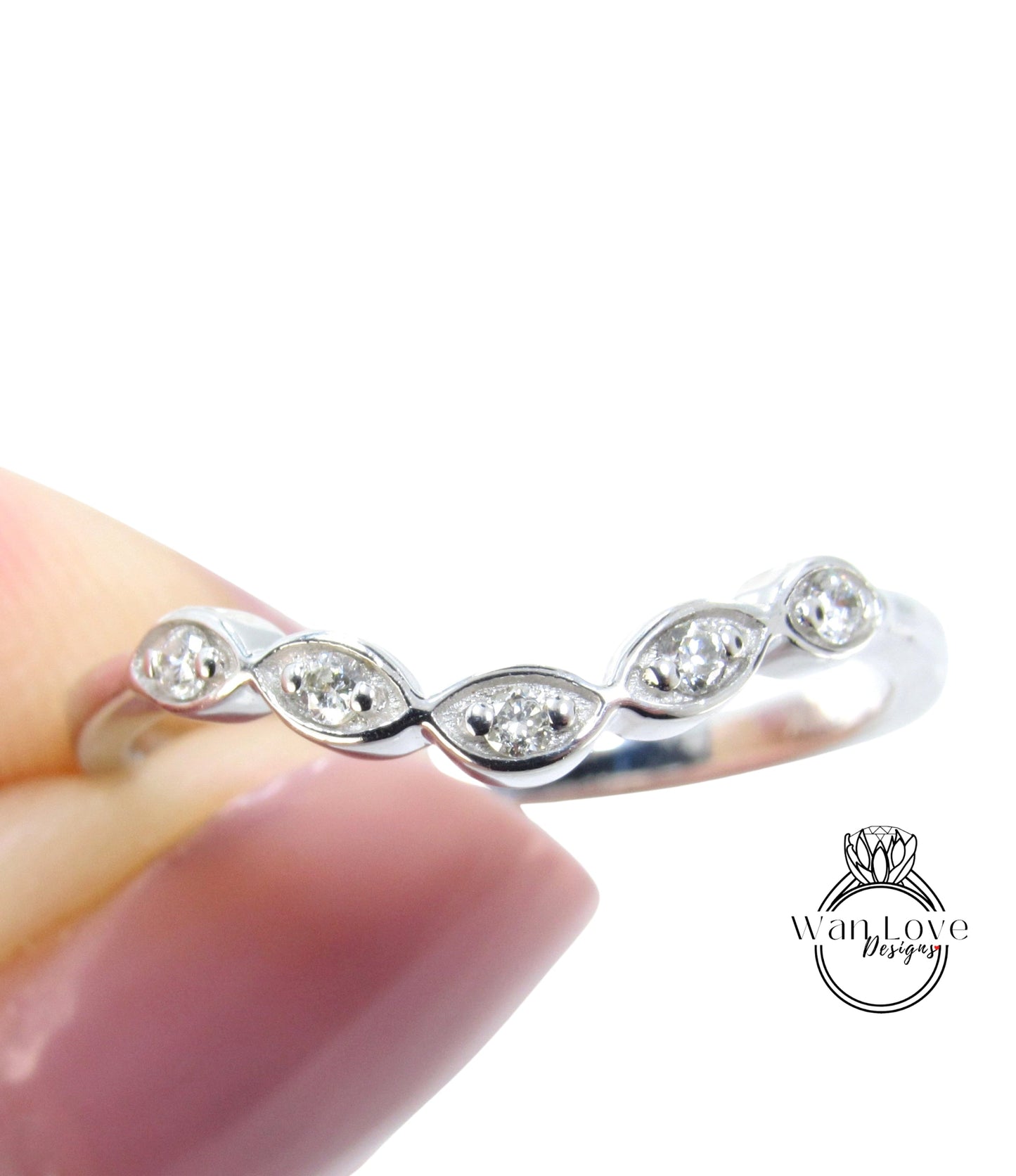 A close-up image of a person's hand holding a silver ring with a row of small diamonds on the band.