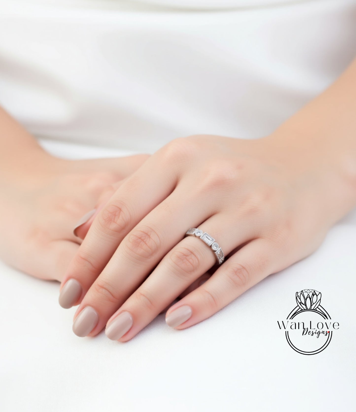 A close-up of a person's hand wearing a diamond ring, resting on a white surface.
