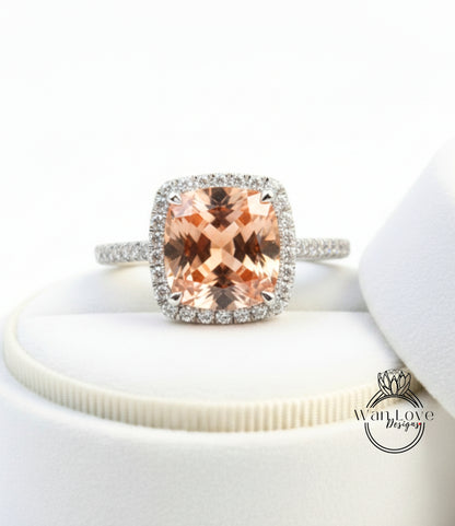 A diamond engagement ring with a large, square-cut peach-colored gemstone set in a halo of smaller diamonds.