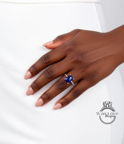 A close-up of a hand wearing a ring with a blue gemstone, resting on a white surface.