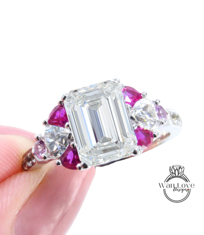 A close-up image of a person's hand holding a diamond engagement ring with a large central diamond surrounded by smaller diamonds and gemstones in various colors, including pink and purple.