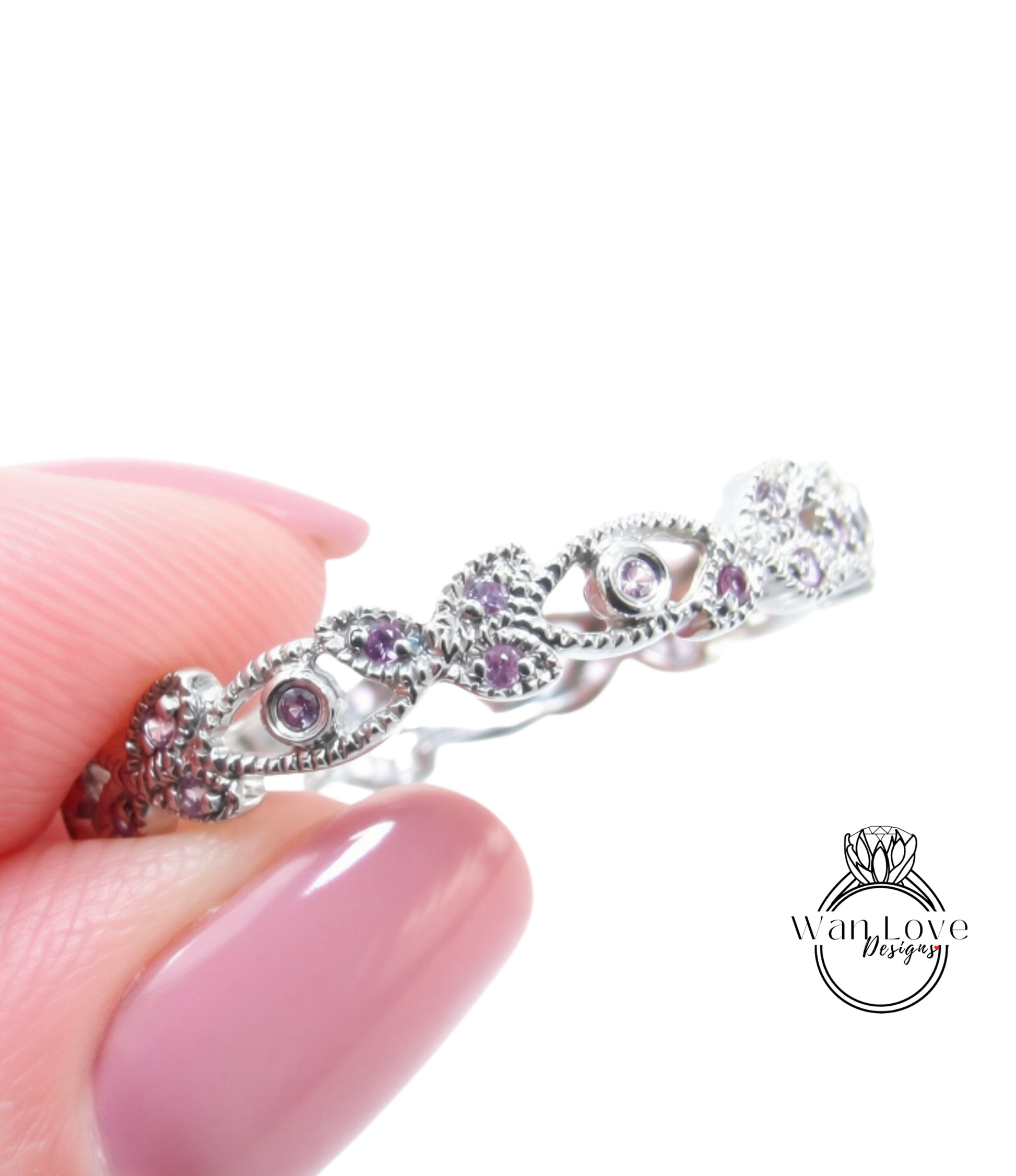 A close-up image of a person's hand holding a silver ring adorned with small purple gemstones.
