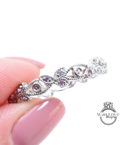 A close-up image of a person's hand holding a silver ring adorned with small purple gemstones.