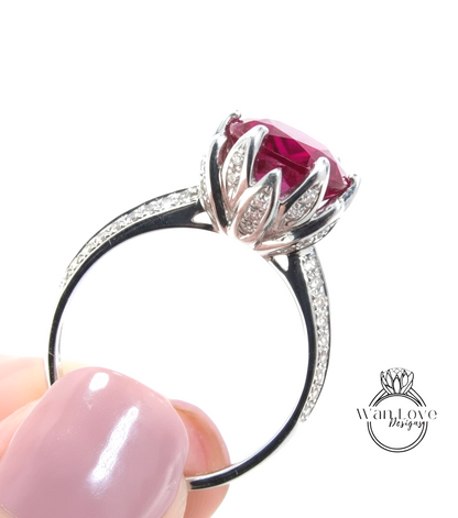 A close-up of a person's hand holding a silver ring with a large, vibrant red gemstone, likely a diamond.