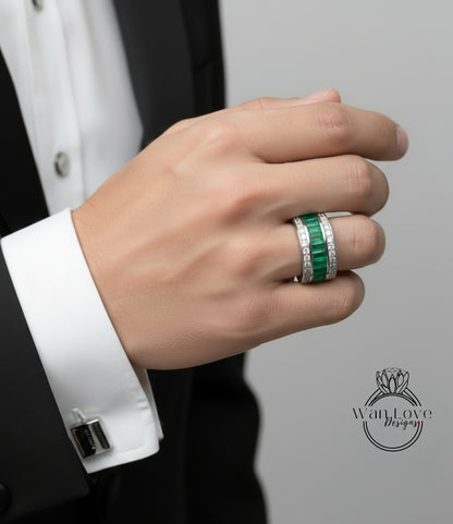A close-up of a person's hand wearing a ring with green gemstones, a cufflink, and a black suit jacket.