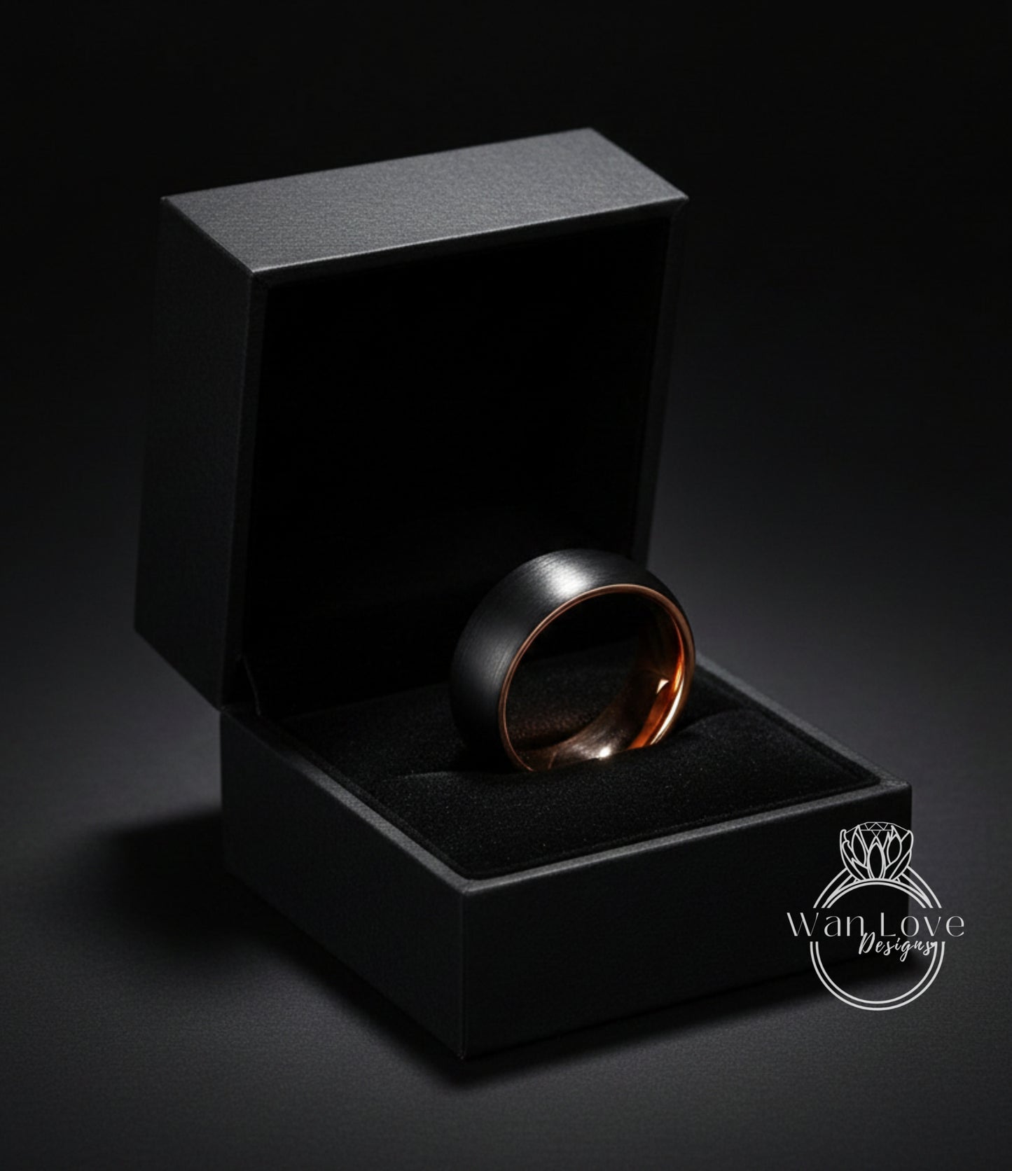 A black jewelry box containing a gold-toned ring, placed on a dark surface.