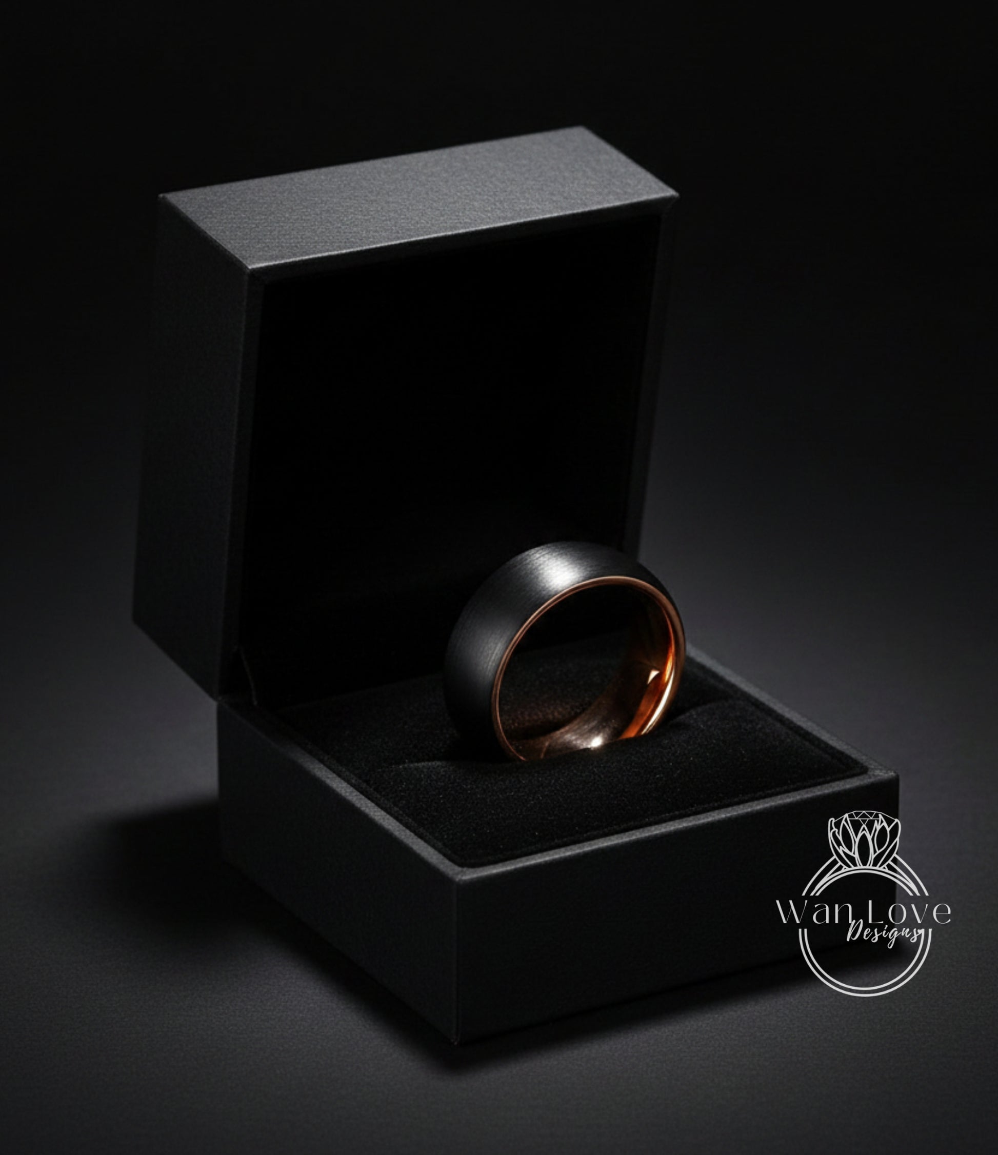 A black jewelry box containing a gold-toned ring, placed on a dark surface.