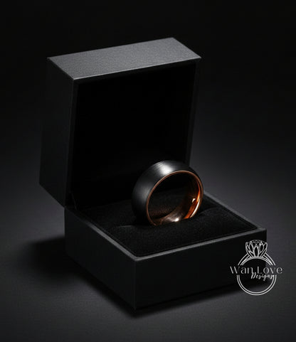 A black jewelry box containing a gold-toned ring, placed on a dark surface.