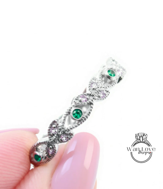 A close-up of a person's hand holding a silver ring adorned with green gemstones.