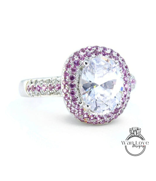 A large, oval-shaped diamond ring with a halo of smaller diamonds around the center stone, set in a silver band with a pinkish-purple accent.