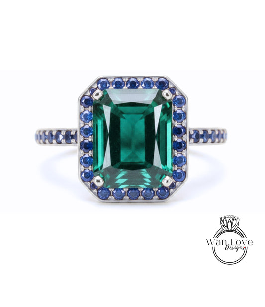 A large, rectangular green gemstone ring with a halo of smaller blue gemstones around the edges.
