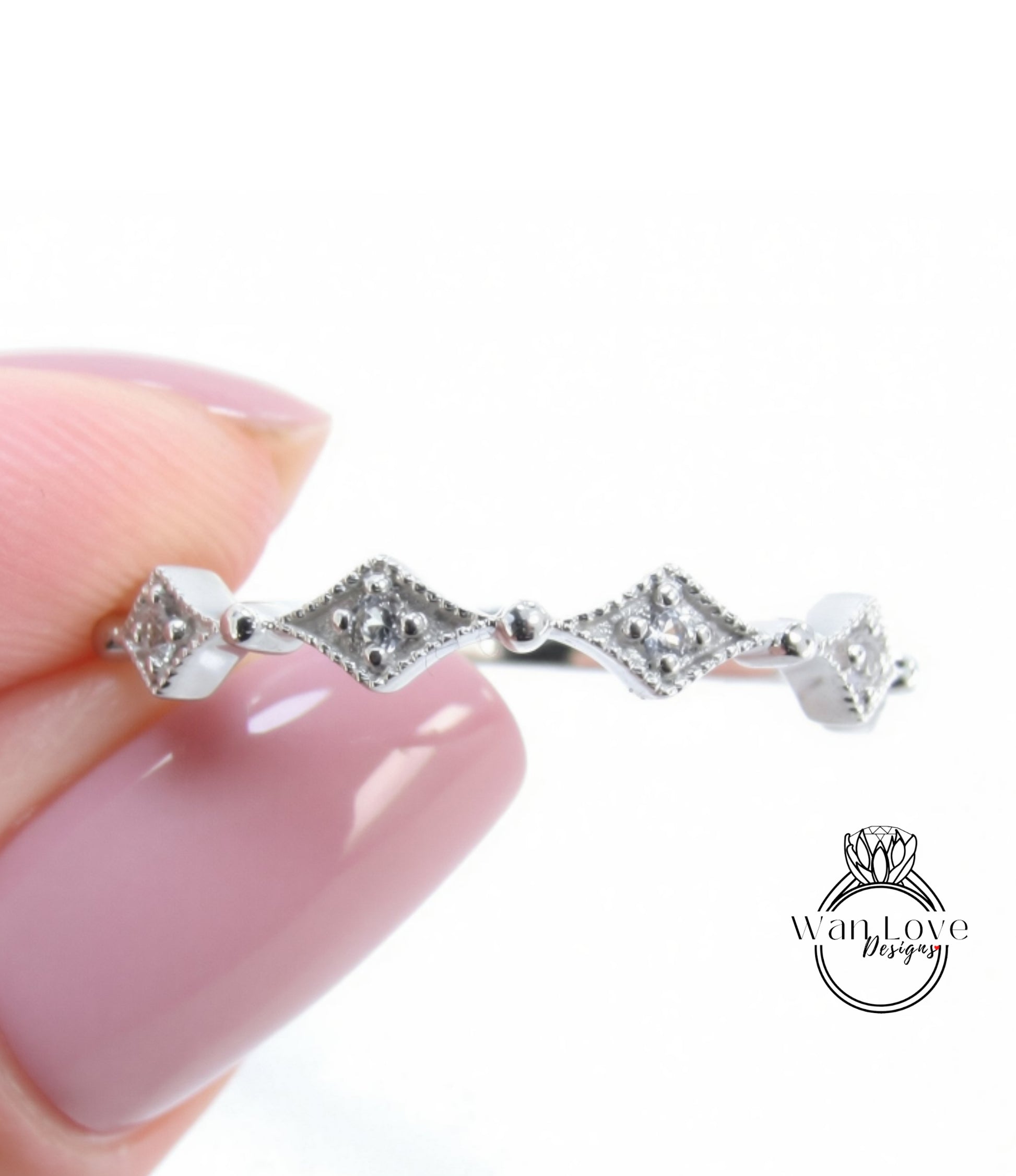 A close-up image of a person's hand holding a silver ring with a row of diamond-shaped stones.