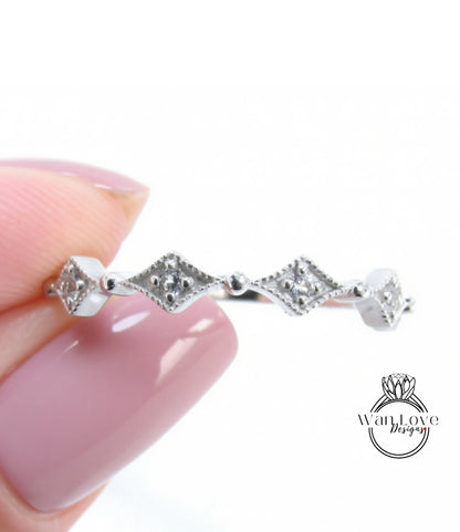 A close-up image of a person's hand holding a silver ring with a row of diamond-shaped stones.