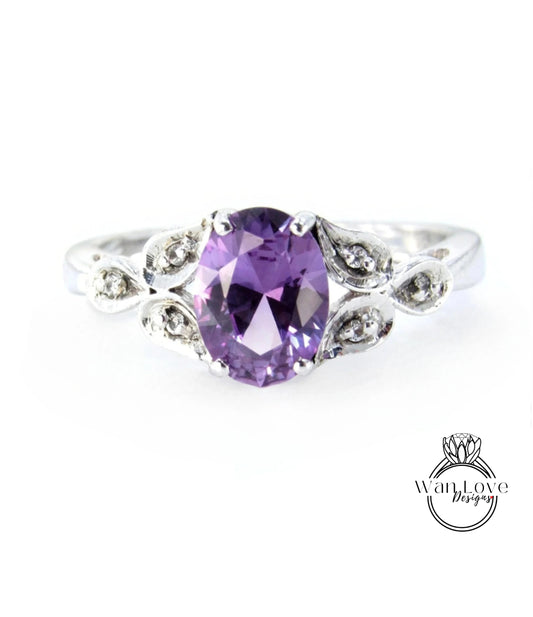 A silver ring with a large oval-shaped purple gemstone, surrounded by small diamonds or crystals.