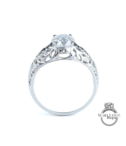A close-up view of a silver engagement ring with a large central diamond and intricate floral designs around the band.
