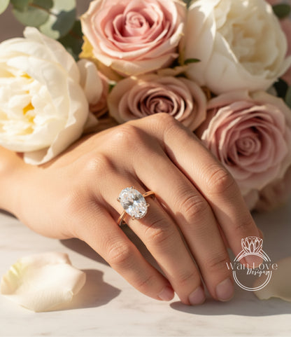 A close-up of a hand wearing a large diamond engagement ring, with a bouquet of pink and white roses in the background.