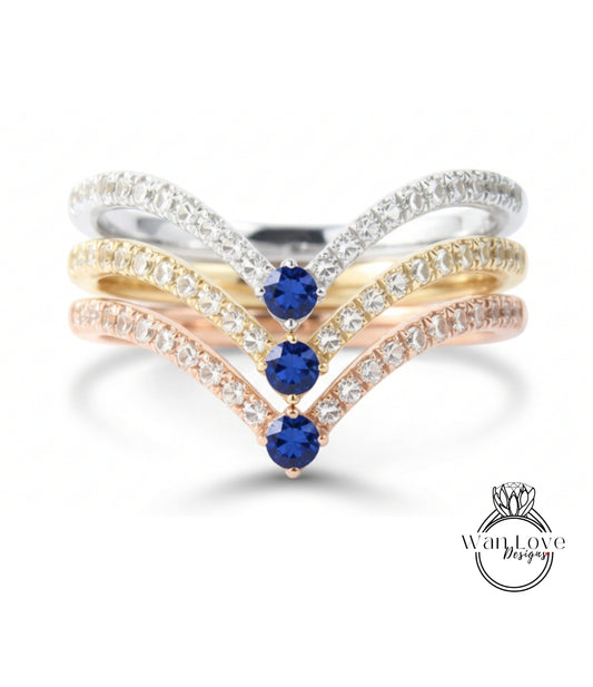 A ring with three blue gemstones set in a diamond-encrusted band, with the gemstones arranged in a v-shape.