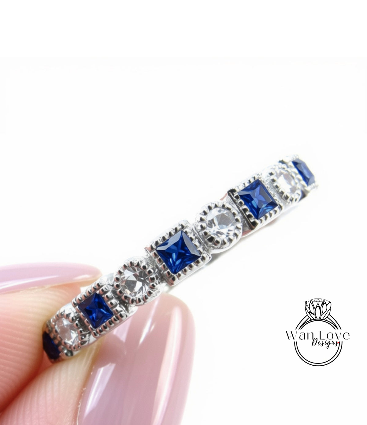 A close-up image of a person's hand holding a silver ring adorned with blue and clear gemstones.
