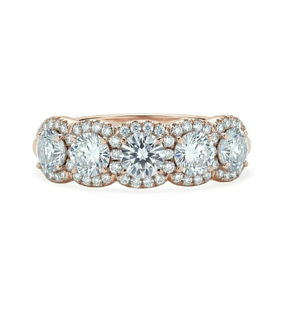 A rose gold ring with a row of five large, clear diamonds set in the center.