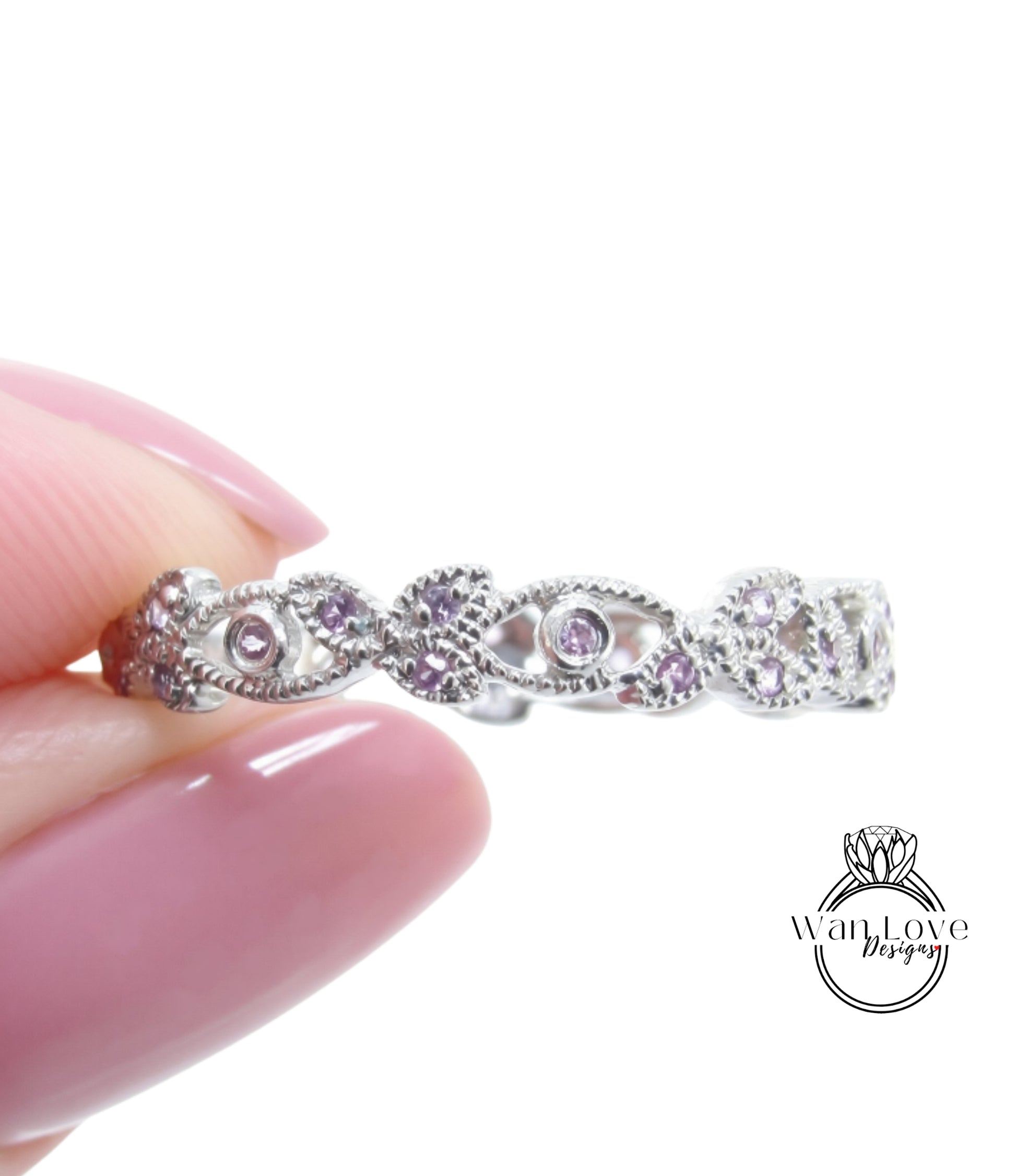 A hand holding a silver ring with a floral design and small purple gemstones.