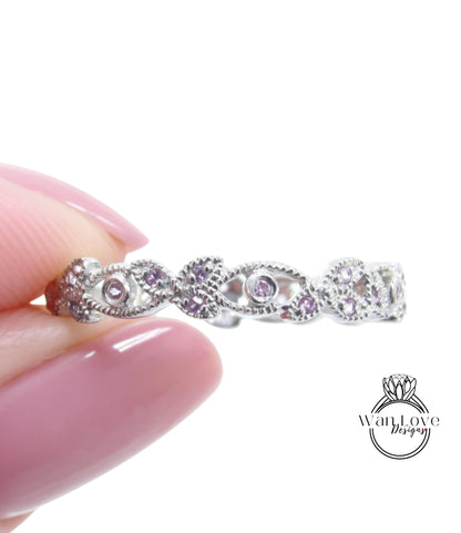 A hand holding a silver ring with a floral design and small purple gemstones.