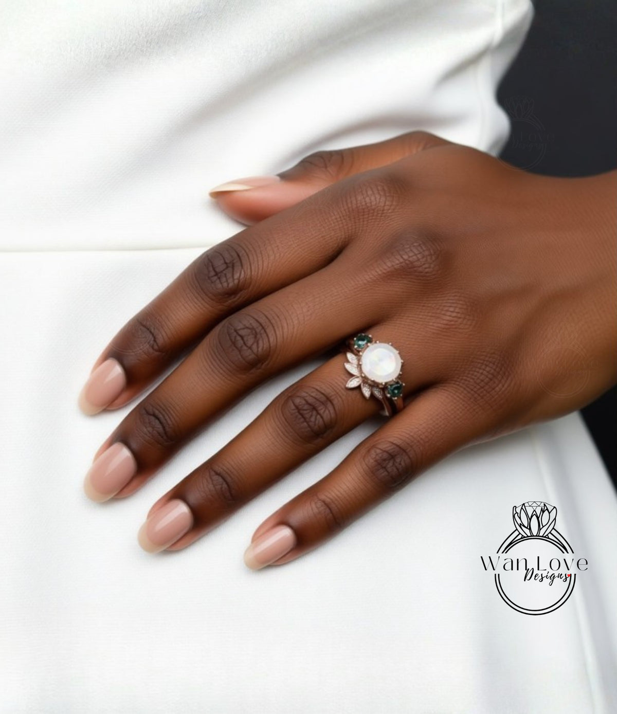 A close-up of a hand wearing a ring with a white stone and green gemstones.
