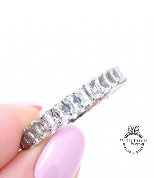 A close-up image of a person's hand holding a silver ring with a row of clear gemstones.