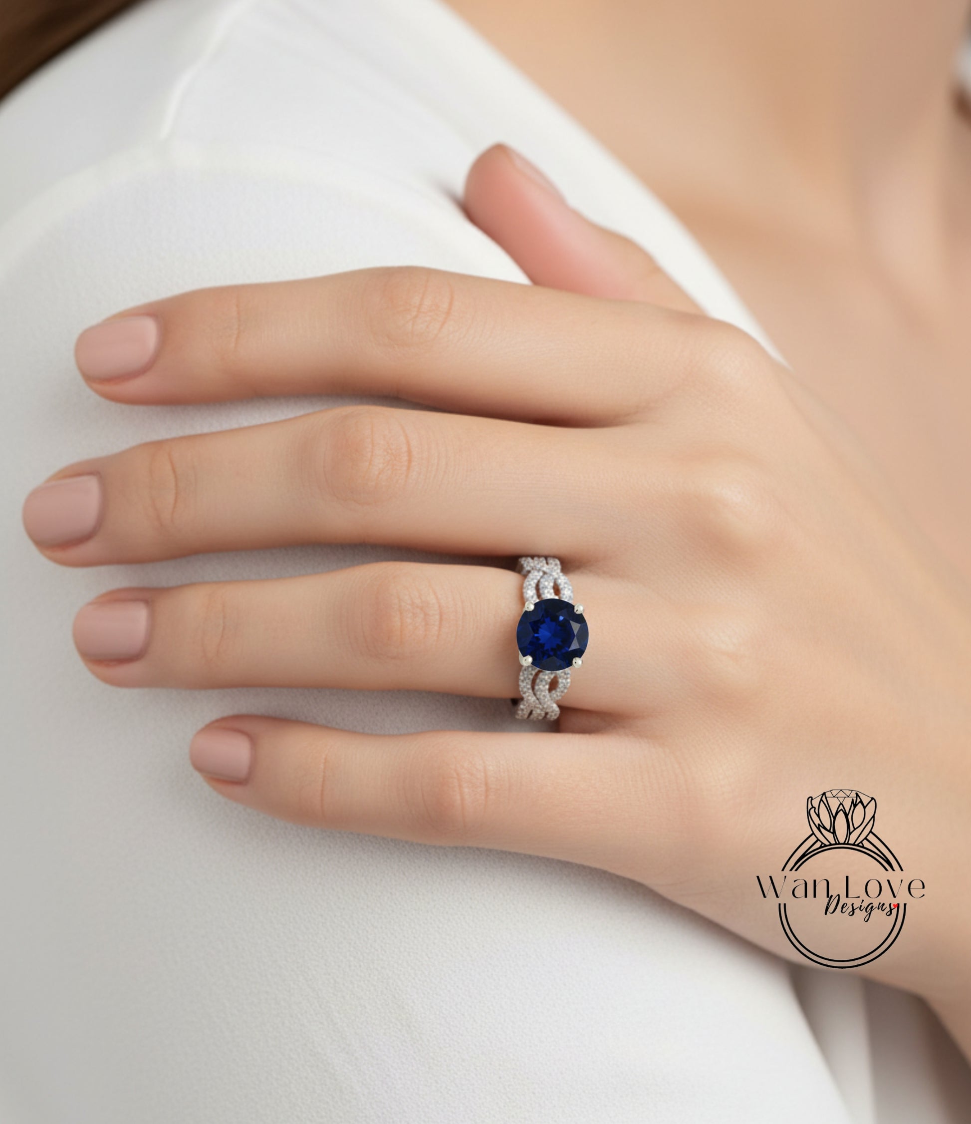 A close-up of a hand wearing a ring with a large blue gemstone, resting on a white surface.