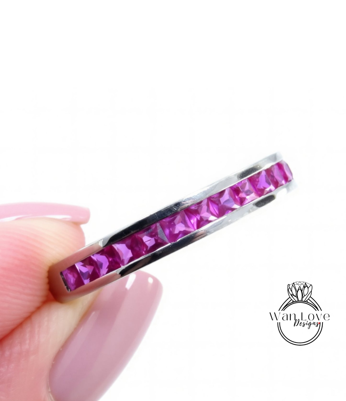A close-up image of a person's hand holding a ring with a row of pink gemstones, likely rubies, set in a silver band.