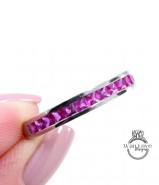 A close-up image of a person's hand holding a ring with a row of pink gemstones, likely rubies, set in a silver band.