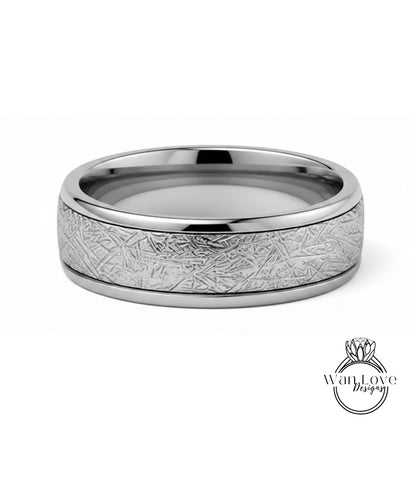 A silver ring with a textured band featuring a metallic, abstract design.