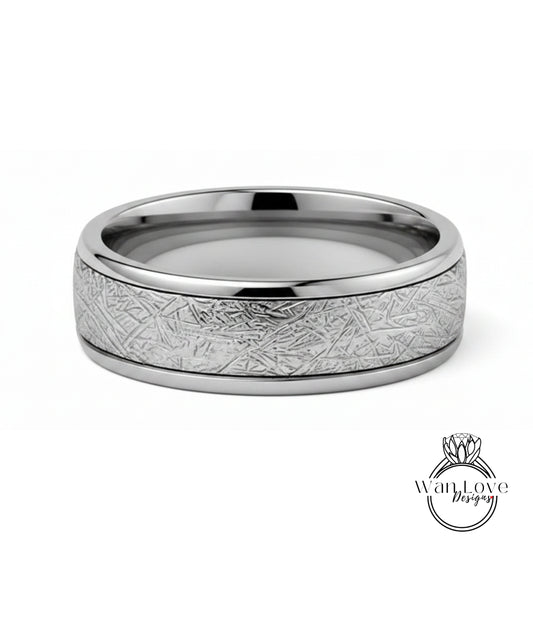 A silver ring with a textured band featuring a metallic, abstract design.