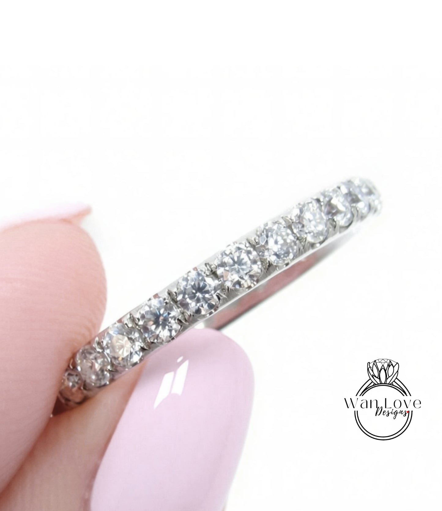 A close-up of a person's hand holding a silver ring with a row of diamonds on it.