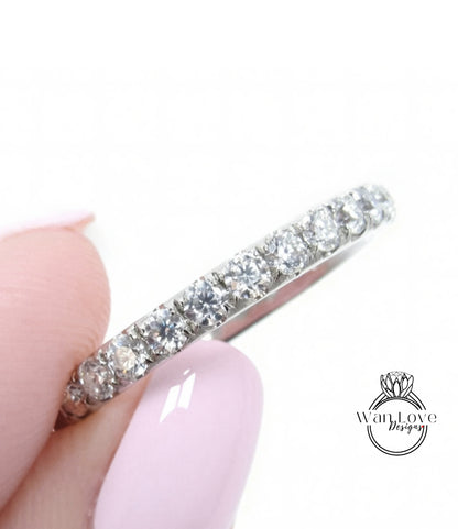 A close-up of a person's hand holding a silver ring with a row of diamonds on it.