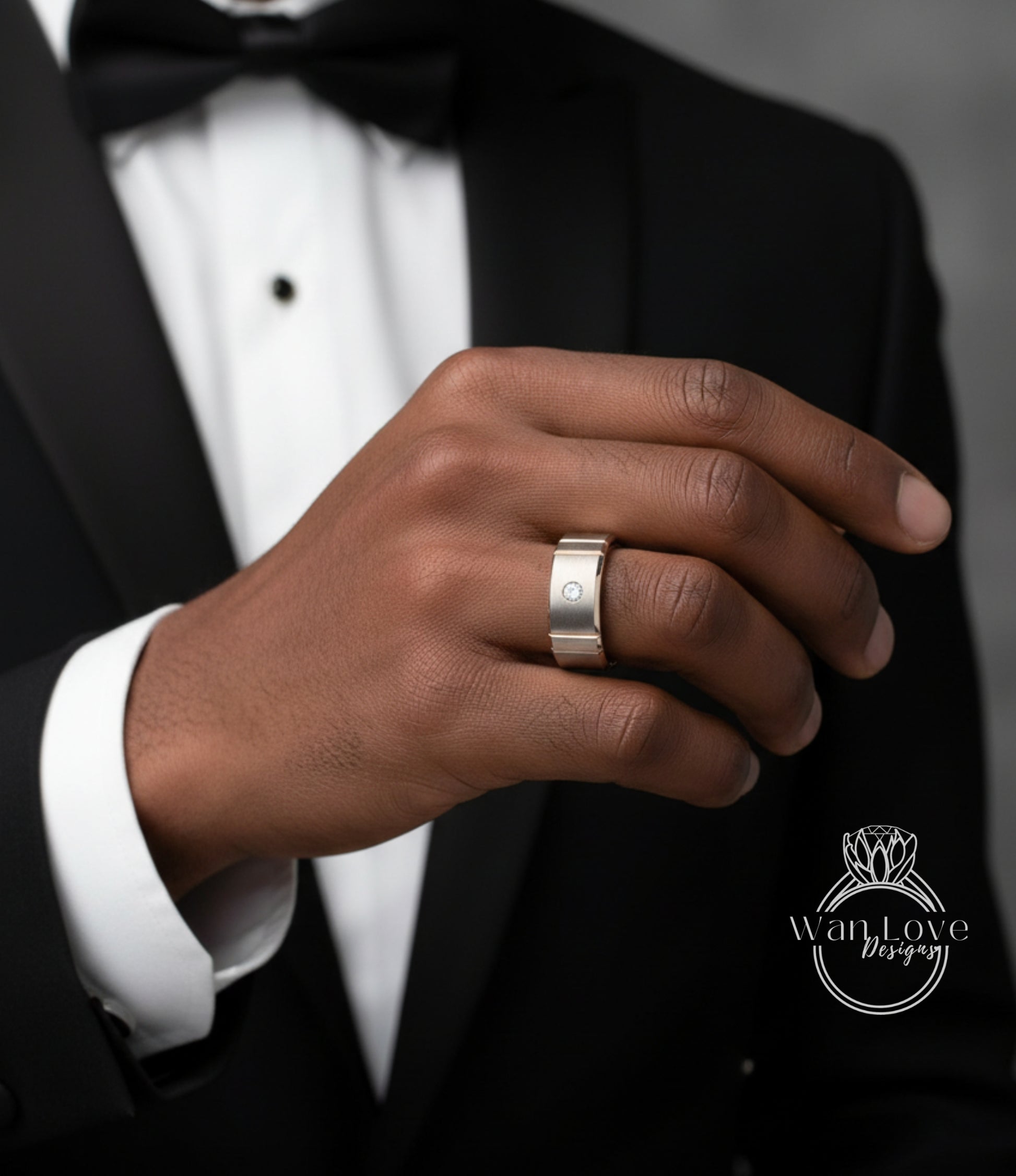 A close-up of a person's hand wearing a ring, with a black suit jacket visible in the background.