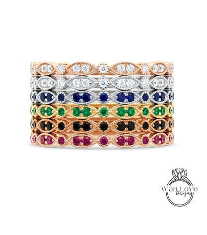 A stack of rings with various colored gemstones, including diamonds and gemstones, set in a rose gold or silver metal band.