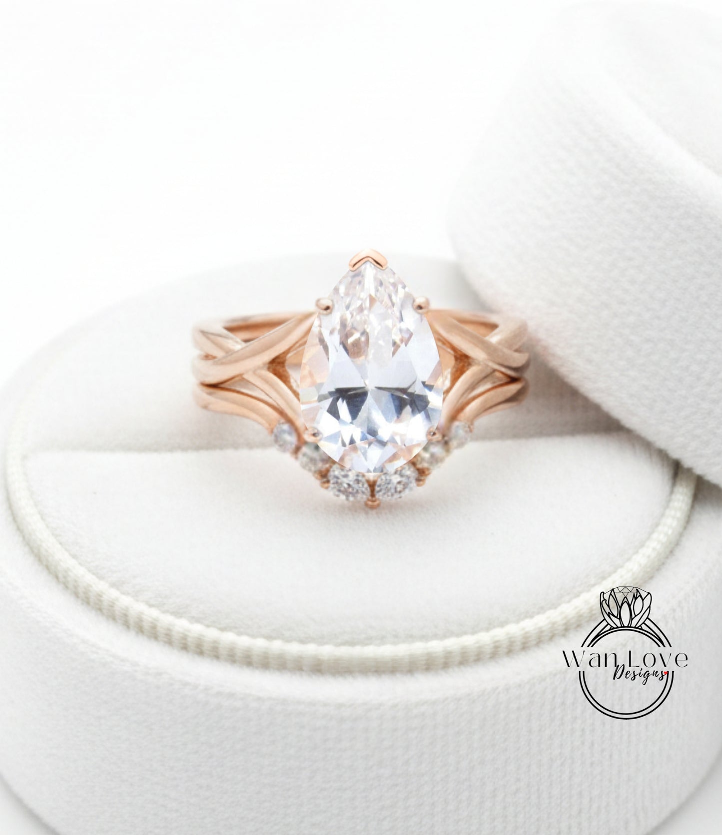 A close-up image of a gold ring with a large pear-shaped diamond set in a ring band, placed on a white fabric background.