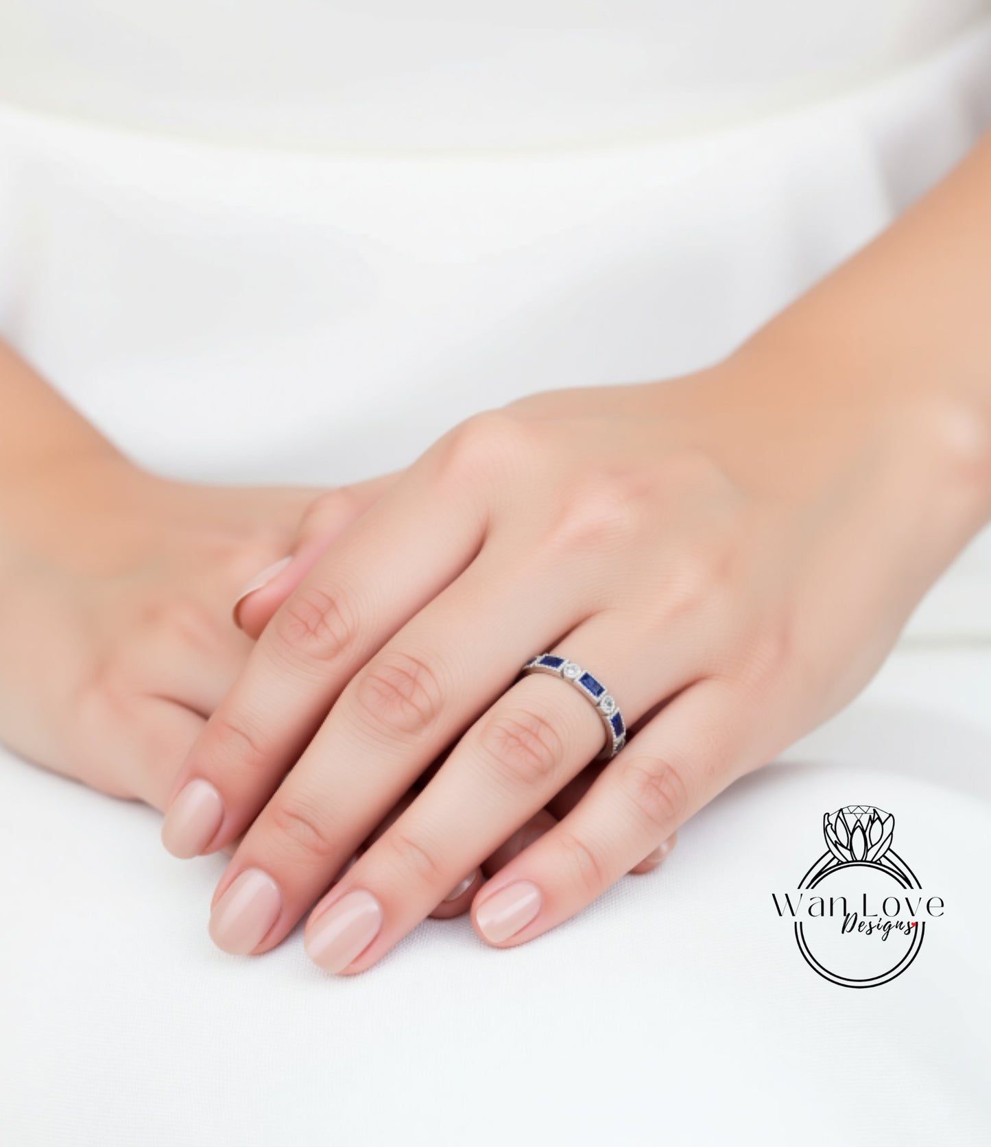 A close-up image of a person's hand wearing a ring with blue gemstones.