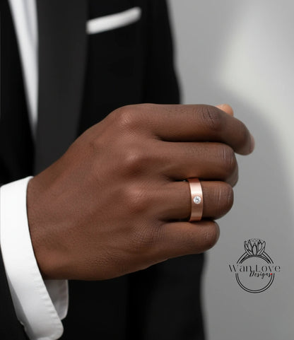 A close-up of a person's hand wearing a gold ring with a diamond, wearing a black suit jacket.