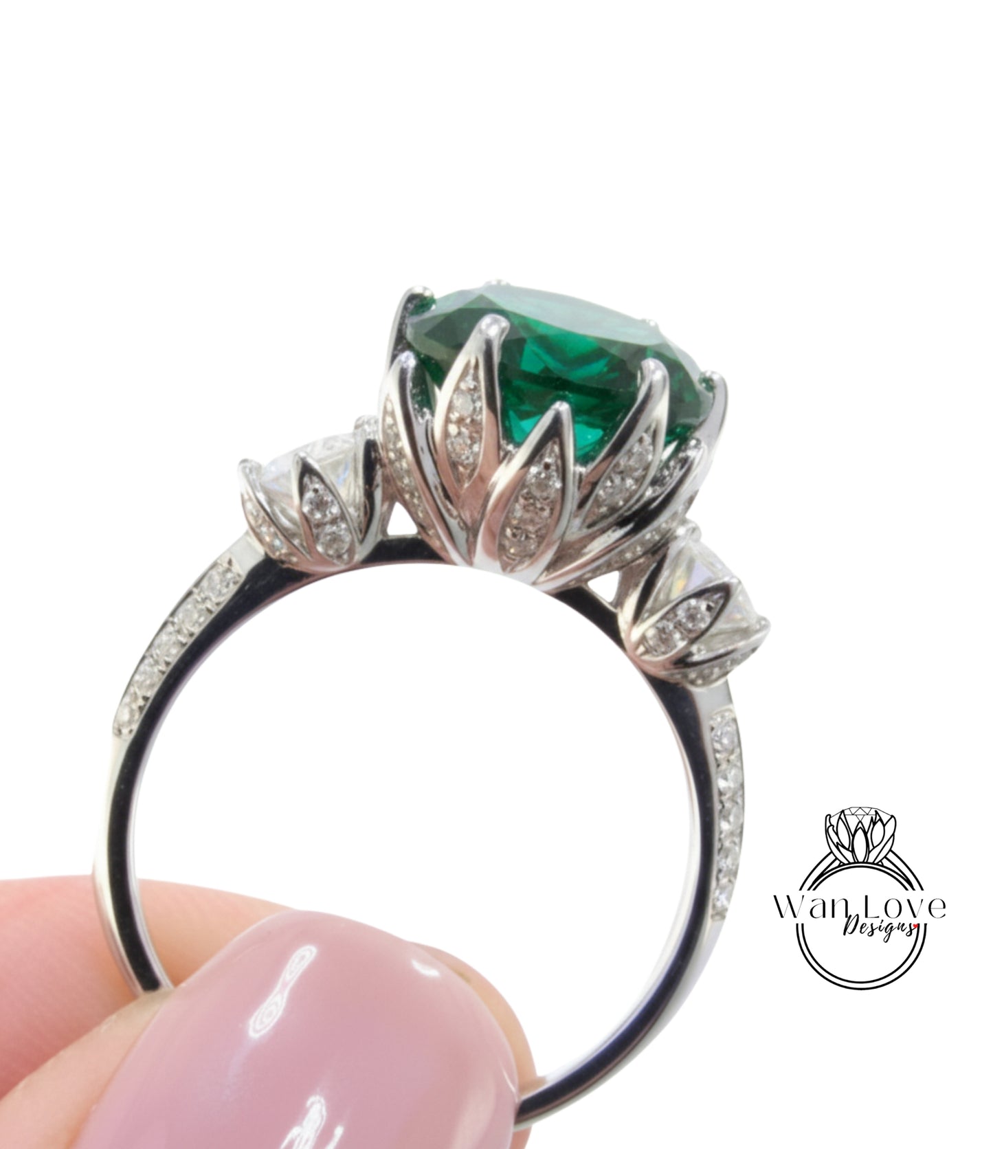 A close-up of a person's hand holding a silver ring with a large, green gemstone.