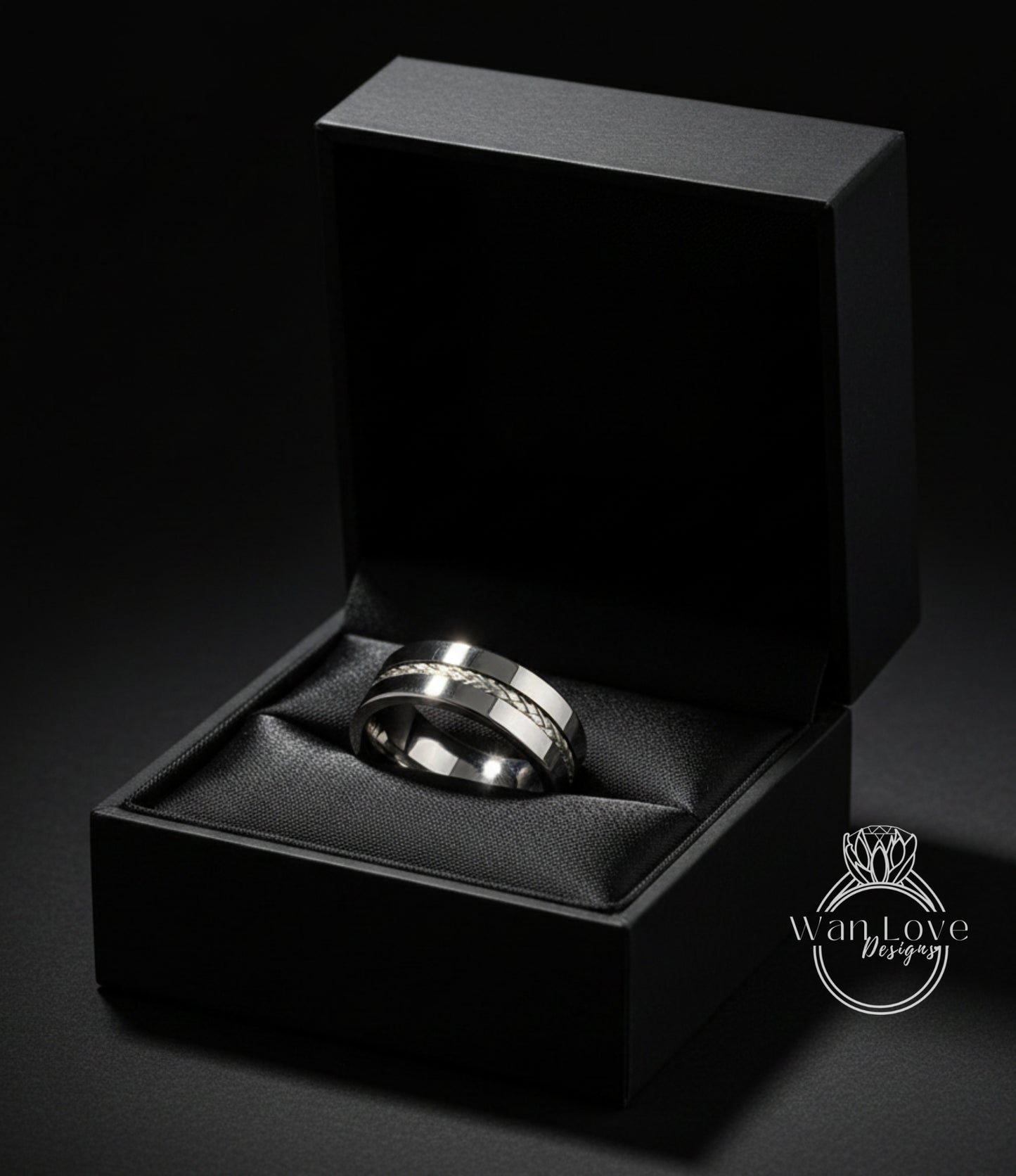 A silver wedding ring is displayed in a black jewelry box against a dark background.