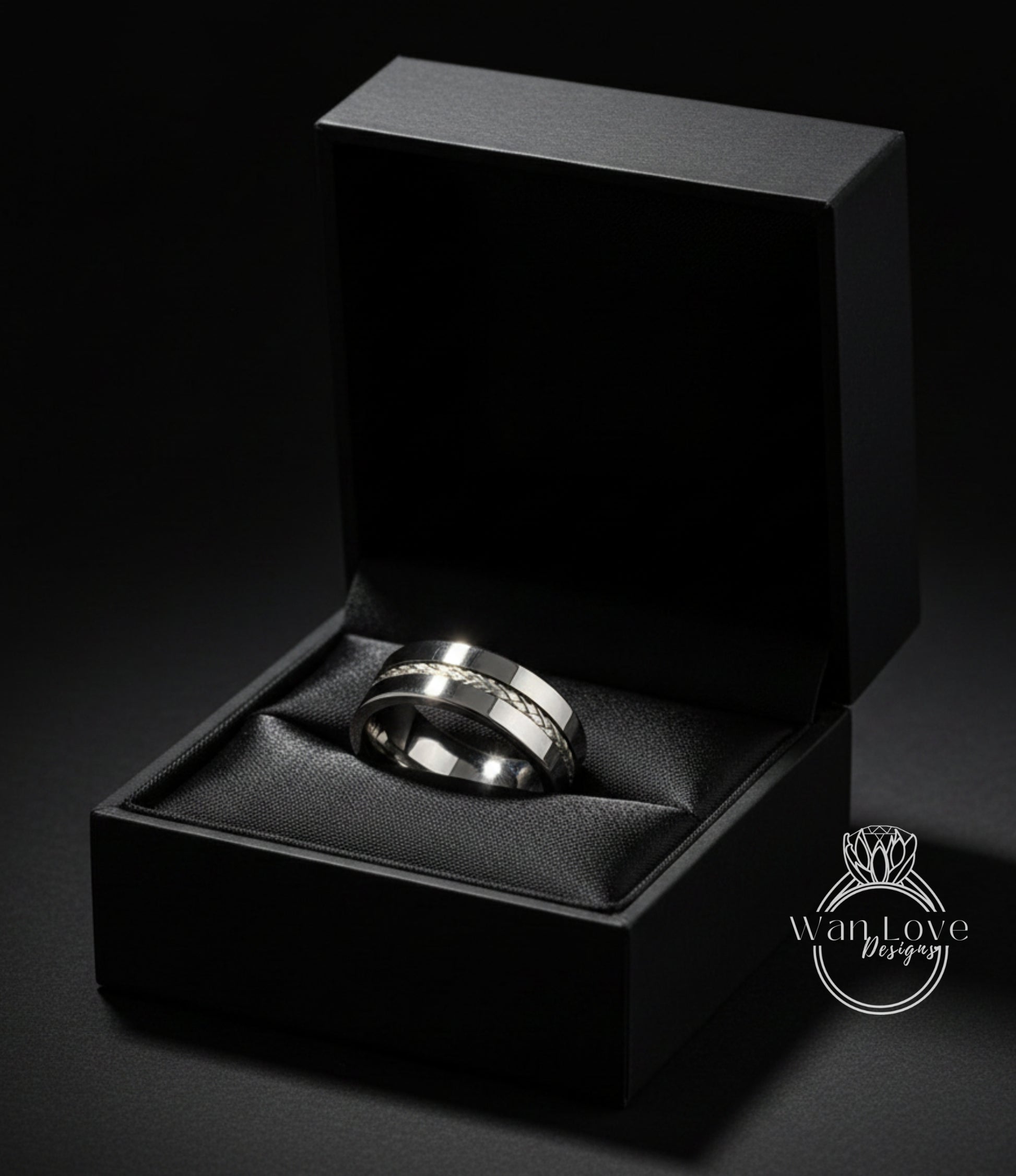 A silver wedding ring is displayed in a black jewelry box against a dark background.