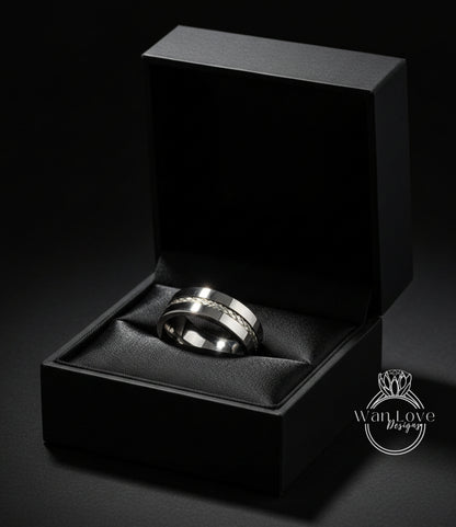 A silver wedding ring is displayed in a black jewelry box against a dark background.