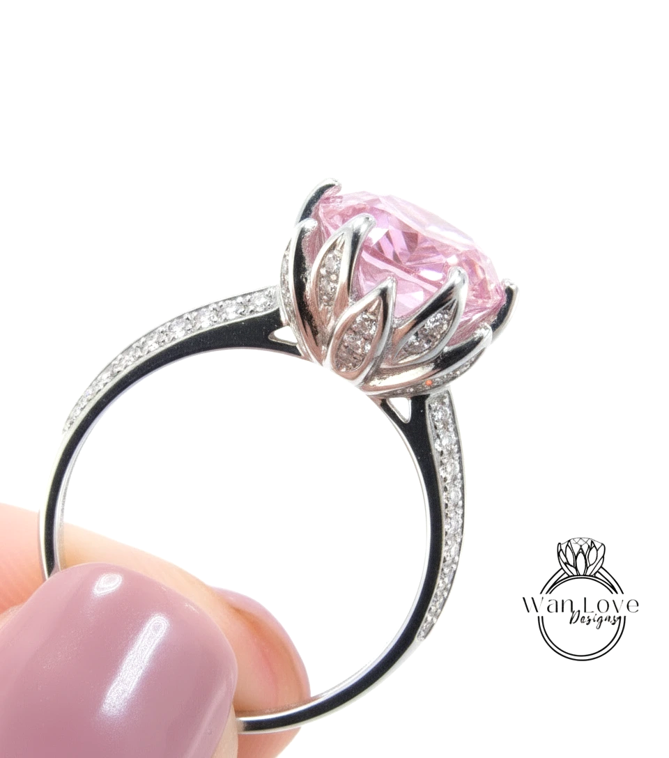 A close-up of a person's hand holding a silver ring with a large pink gemstone, likely a diamond, set in a decorative metal band.