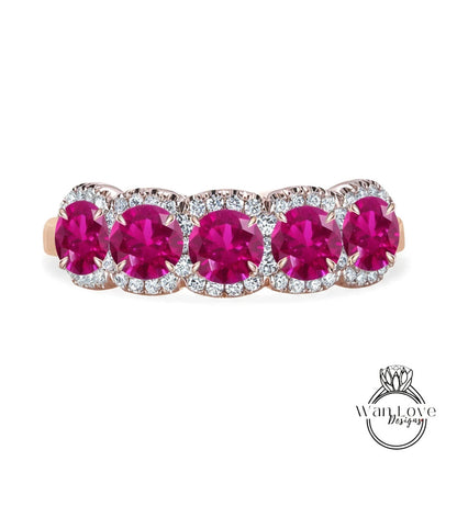 A pink gemstone ring with a row of five large, round, deep red gemstones set in a halo of smaller diamonds.