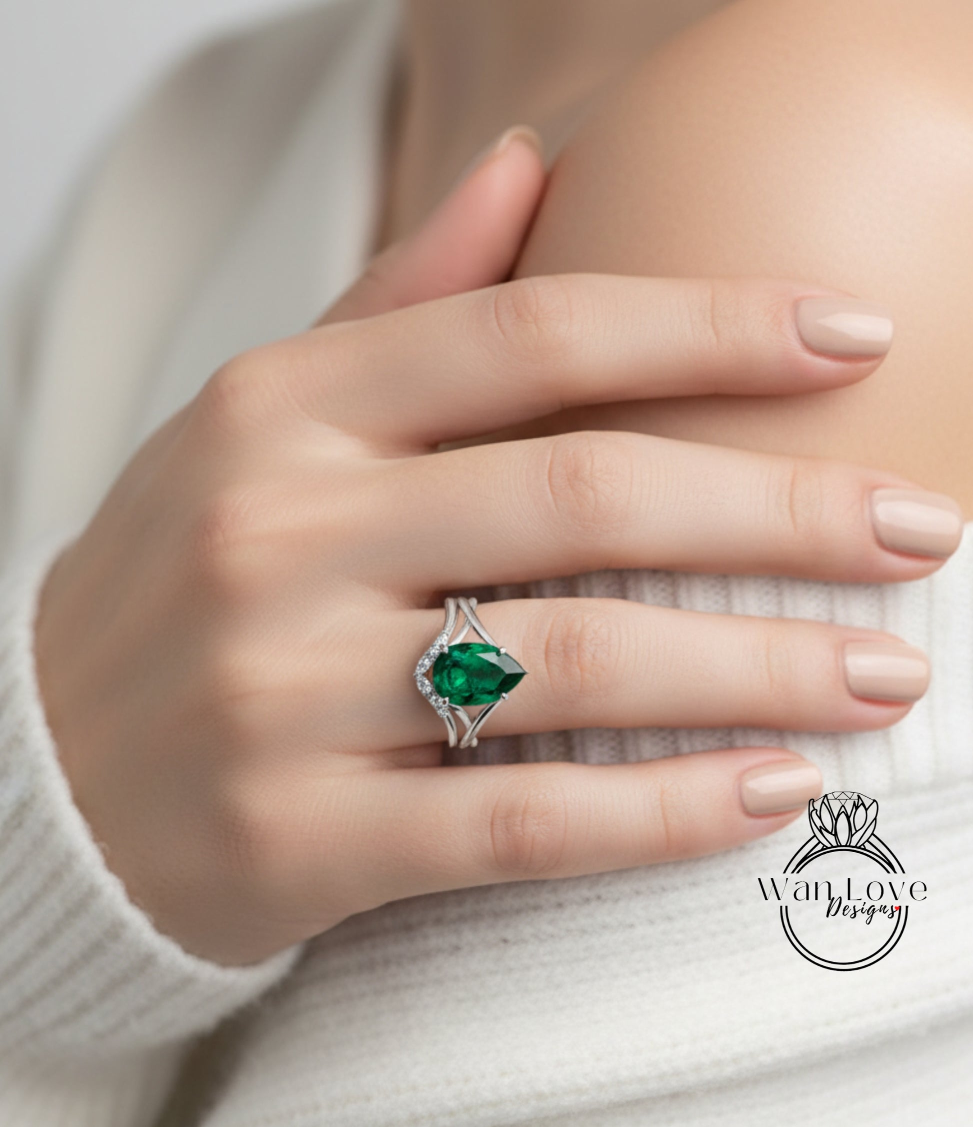 A close-up of a person's hand wearing a ring with a large green gemstone, resting on a white sweater.