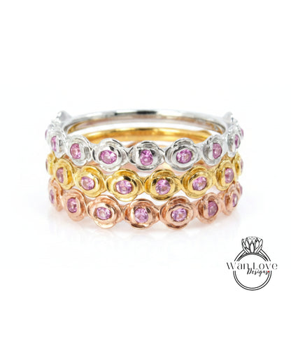 A stack of rings with pink gemstones in various colors, including silver, gold, and rose gold.